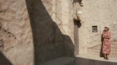 Dubai 'de Al Seef Parkı' nı gezen etnik giysili ve şapkalı genç bir kadın. Geleneksel Emirati mimarisi ve modern atmosferiyle çevrelenmiş olan sanatçı, Dubai Dereleri kültür mirasının cazibesine sahip..