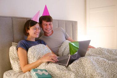 Genç bir ailenin doğum günü kutlaması sırasında dizüstü bilgisayarında akrabalarıyla görüntülü sohbet etmesi. Gülümseyen ve neşeli, sevdikleriyle bağ kuran, evlerinin rahatlığından özel bir vesile paylaşan.