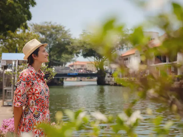 Malacca, Malezya 'nın canlı sokaklarını keşfeden etnik giysili ve şapkalı genç bir kadın. Kültürel miras, renkli mimari ve tropikal cazibenin bir karışımı. Mükemmel seyahat ve yaşam tarzı anları.