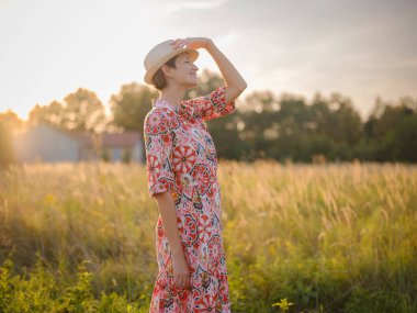 Yaz sonlarında Avrupa 'nın pitoresk alanlarında yürüyen genç bir kadın. Altın güneş ışığı, yemyeşil yemyeşil ve sakin kırsal atmosfer huzurlu bir kırsal alan yaratır..