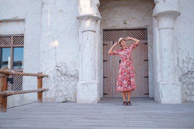 Dubai 'de Al Seef Parkı' nı gezen etnik kıyafetli ve şapkalı genç bir kadın. Geleneksel Emirati mimarisi ve modern atmosferiyle çevrelenmiş Dubai Deresi 'nin kültürel mirasının cazibesine sahip..