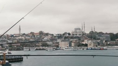 İstanbul, Türkiye - 3 Aralık 2023. Galata Köprüsü 'nde oltaları olan balıkçılar. Tarihi ve modern şehrin arka planına çubuklarla bakan balıkçıların manzara görüntüsü.