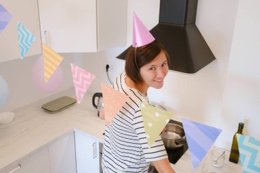 Genç bir kadın, rahat bir atmosfer ve şenlikli dekorasyonla çevrili olarak doğum gününü evde kutluyor. Şenlikli bir akşam yemeği pişiriyor, lezzetli bir makarna.