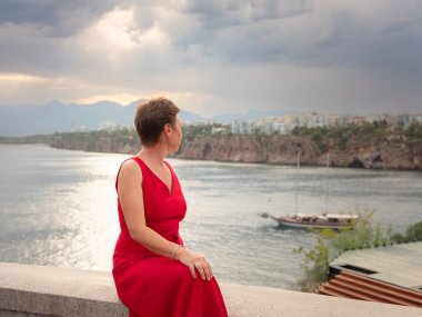 Sıcak yaz akşamları Antalya 'nın dar sokaklarında kırmızı elbiseli bir kadın yürüyor. Tarihsel atmosfer ve Akdeniz cazibesi barışçıl seyahat deneyimleri yaratır. Eski liman ve kentte görünüm