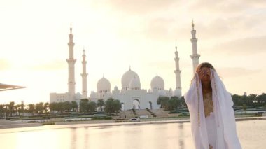 Abu Dabi 'deki Şeyh Zayed Büyük Camii yakınlarındaki Wahat Al Karama' daki geleneksel Arap elbiseli kadın, gün batımında kültürel zarafet ve ikonik İslami mimari sergiliyor..