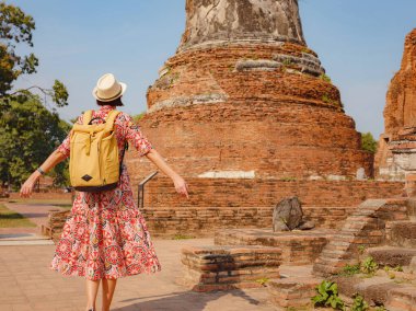 Tayland 'ın Ayutthaya kentinde tarihi parkı keşfetmek için giyinmiş genç bir bayan turist. Antik tapınaklar ve heykellerle çevrelenmiş, barışçıl atmosfer ve zengin kültür mirasının tadını çıkarıyor. Arkadan görünüm
