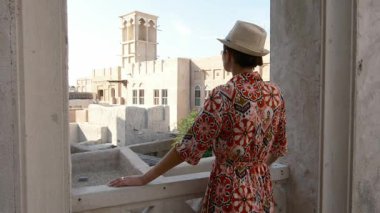 Dubai 'de Al Seef Parkı' nı gezen etnik giysili ve şapkalı genç bir kadın. Geleneksel Emirati mimarisi ve modern atmosferiyle çevrelenmiş olan sanatçı, Dubai Dereleri kültür mirasının cazibesine sahip..