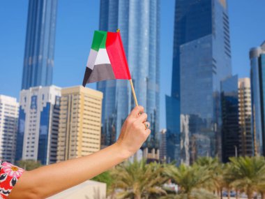 Abu Dabi siluetine karşı kadın eli, BAE 'nin küçük bayrağını tutuyor. BAE ulusal kutlama ruhunun fotoğrafı..