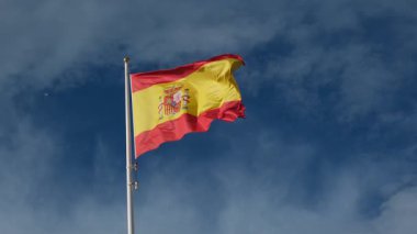 İspanyol bayrağı zarif bir şekilde mavi gökyüzüne doğru dalgalanıyor. Spains kültürel kimliğinin özünü yakalayan ulusal gurur, birlik ve mirasın güçlü bir sembolü.