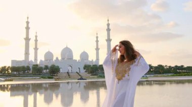 Abu Dabi 'deki Şeyh Zayed Büyük Camii yakınlarındaki Wahat Al Karama' daki geleneksel Arap elbiseli kadın, gün batımında kültürel zarafet ve ikonik İslami mimari sergiliyor..