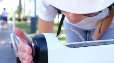 Genç bir kadın Abu Dabi 'deki parktaki bir çeşmeden su içiyor. Palmiye ağaçları ve yeşilliklerle çevrili. Sakin bir vahada güneşli bir günde ferahlatıcı bir an..