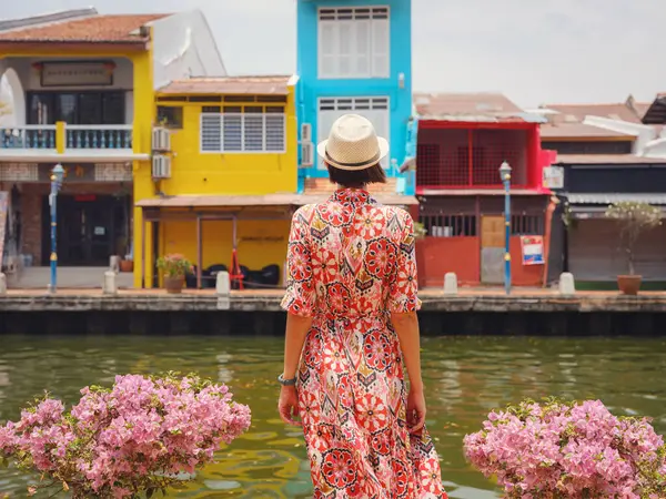 Malacca, Malezya 'nın canlı sokaklarını keşfeden etnik giysili ve şapkalı genç bir kadın. Kültürel miras, renkli mimari ve tropikal cazibenin bir karışımı. Mükemmel seyahat ve yaşam tarzı anları.
