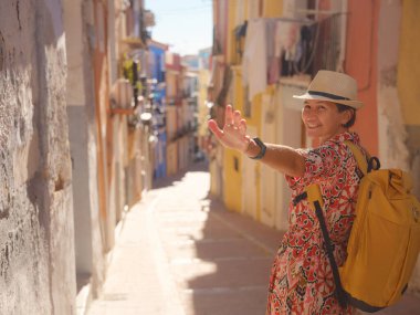 İspanyol kıyı kasabası La Vila Joiosa ya da Villajoyosa 'nın renkli caddelerinde gezen kadın. Güneşli kış atmosferi Akdeniz mimarisinin ve sakin deniz yaşamının cazibesini vurguluyor