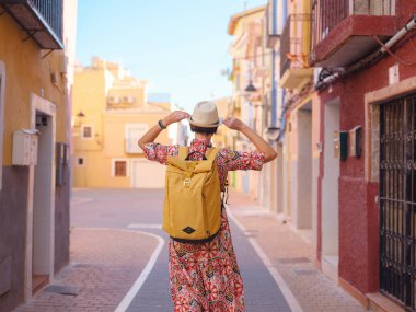 İspanyol kıyı kasabası La Vila Joiosa 'nın renkli sokaklarında gezen kadın. Güneşli kış atmosferi Akdeniz mimarisinin cazibesini ve sakin sahil yaşamını ön plana çıkarıyor.