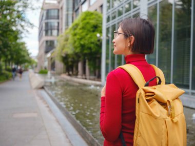 Turist kadın modern Frankfurt 'u keşfediyor, çağdaş mimari, gökdelenler ve kentsel alanlarla hareketli caddelerde yürüyor, modern yan tarafların canlı atmosferinin tadını çıkarıyor..