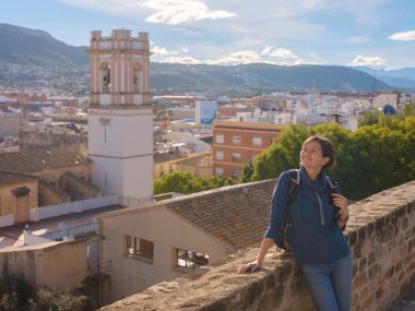 Denia, Alicante, İspanya 'da tarihi şatoyu keşfeden genç bir kadın, aşağıdaki kasabanın manzarası, daha serin mevsim arkaplanlarına karşı. Tarihin ve sükunetin zamansız ortamında harmanlanması.