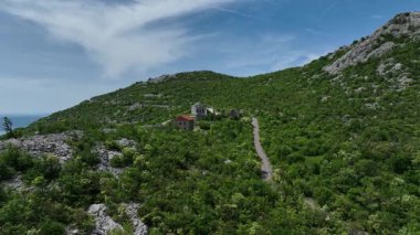 Tulove Grede dağları yakınlarındaki St. Francis kilisesinin insansız hava aracı görüntüsü. Tulove Grede Dağı 'nın yanındaki küçük taş kilise, uzak Hırvat manzarasındaki yaban tepeleri ve bahar bitkileri tarafından çerçevelenmiş yukarıdan görülüyor.