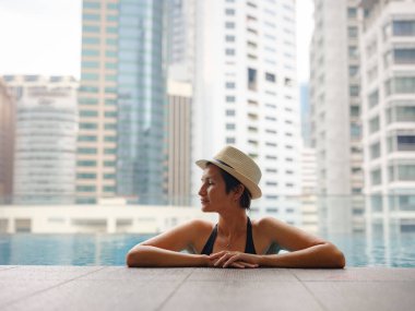 Kuala Lumpur Oteli 'nde havuz başında dinlenen Asyalı genç bir kadın. Etrafı gökdelenlerle çevrili, hareketli şehir ortamında boş vakitlerin tadını çıkarıyor..