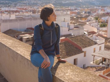 Denia, Alicante, İspanya 'da tarihi şatoyu keşfeden genç bir kadın, aşağıdaki kasabanın manzarası, daha serin mevsim arkaplanlarına karşı. Tarihin ve sükunetin zamansız ortamında harmanlanması.