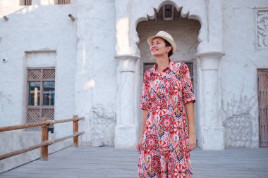 Dubai 'de Al Seef Parkı' nı gezen etnik kıyafetli ve şapkalı genç bir kadın. Geleneksel Emirati mimarisi ve modern atmosferiyle çevrelenmiş Dubai Deresi 'nin kültürel mirasının cazibesine sahip..