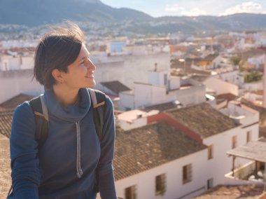 Denia, Alicante, İspanya 'da tarihi şatoyu keşfeden genç bir kadın, aşağıdaki kasabanın manzarası, daha serin mevsim arkaplanlarına karşı. Tarihin ve sükunetin zamansız ortamında harmanlanması.