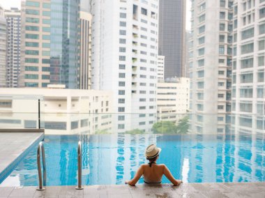 Kuala Lumpur Oteli 'nde havuz başında dinlenen Asyalı genç bir kadın. Etrafı gökdelenlerle çevrili, hareketli şehir ortamında boş vakitlerin tadını çıkarıyor..