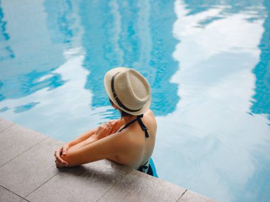 Kuala Lumpur Oteli 'nde havuz başında dinlenen Asyalı genç bir kadın. Etrafı gökdelenlerle çevrili, hareketli şehir ortamında boş vakitlerin tadını çıkarıyor..