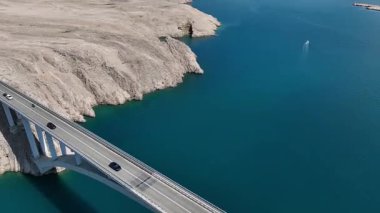 Mavi Adriyatik Denizi 'nin karşısındaki Köprü Pag Adası. Hırvatistan 'ı Pag Adası' na bağlayan köprü geniş çaplı insansız hava aracı görüntüsü. Çarpıcı deniz, kayalık kıyı şeridi, ılık bahar ışığı tonları dramatik bir kompozisyon oluşturur..