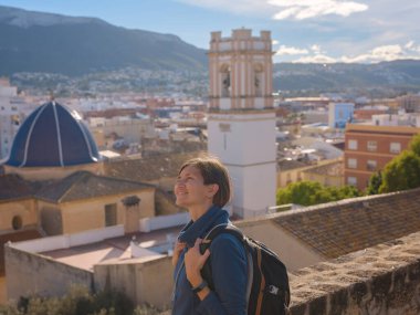 Denia, Alicante, İspanya 'da tarihi şatoyu keşfeden genç bir kadın, aşağıdaki kasabanın manzarası, daha serin mevsim arkaplanlarına karşı. Tarihin ve sükunetin zamansız ortamında harmanlanması.