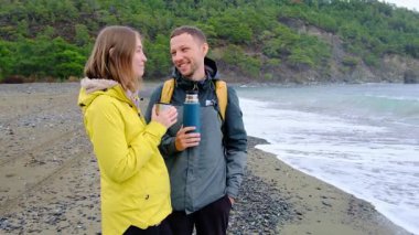 Genç çift kışın deniz kenarında çay içer. Bulutlu gökyüzü, hafif rüzgar, soğuk hava, sıcak içecekler. Sakin sakin bir an, günlük hayattan rahat bir kaçış, doğada derin bir bağ..