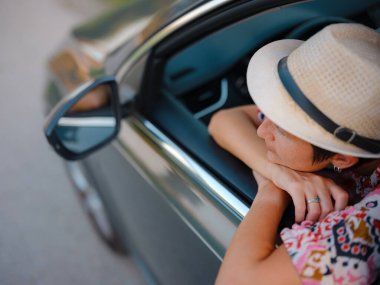 Kırmızı etnik giysili ve şapkalı gezgin kadın yazın Hırvatistan 'ın manzaralı kırsalında araba sürüyor. Etrafı yemyeşil tarlalar ve ormanlarla çevrili, huzurlu ve maceralı bir yolculuktan hoşlanıyor.