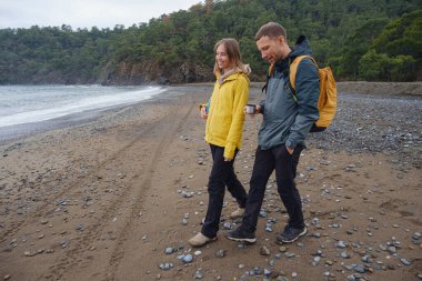 Çiftler Türk kıyı şeridini seviyor. Taşlarda oturmak, deniz dalgalarını izlemek, birlikte dinlenmek, sakin mavi suyun yanında, yumuşak kış ışığı altında romantik bir an..