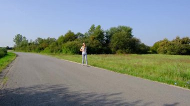 Güneşli bir günde asfalt yolda yürüyen bir kadın yürüyüş macerasına girişiyor. Manzaralı manzaralar ve açık hava ile çevrelenmiş, seyahatin ve açık hava deneyiminin tadını çıkarıyor..
