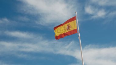 İspanyol bayrağı zarif bir şekilde mavi gökyüzüne doğru dalgalanıyor. Spains kültürel kimliğinin özünü yakalayan ulusal gurur, birlik ve mirasın güçlü bir sembolü.