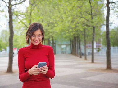 Bahar günü Frankfurt 'ta yürüyen ve elinde cep telefonu olan güzel bir kadın. Şehir yaşam tarzı konsepti. Sosyal ağları kontrol edin, mesaj ya da kitap oteli gönderin, güven ve profesyonellik yaygınlığı