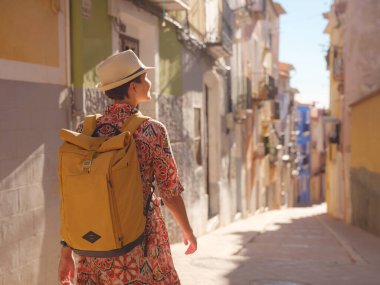 İspanyol kıyı kasabası La Vila Joiosa 'nın renkli sokaklarında gezen kadın. Güneşli kış atmosferi Akdeniz mimarisinin cazibesini ve sakin sahil yaşamını ön plana çıkarıyor.