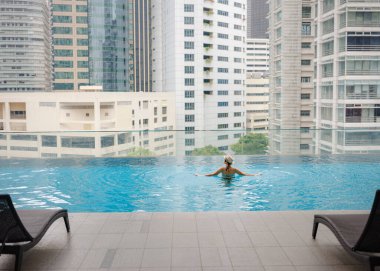 Kuala Lumpur Oteli 'nde havuz başında dinlenen Asyalı genç bir kadın. Etrafı gökdelenlerle çevrili, hareketli şehir ortamında boş vakitlerin tadını çıkarıyor..
