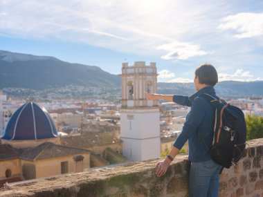 Denia, Alicante, İspanya 'da tarihi şatoyu keşfeden genç bir kadın, aşağıdaki kasabanın manzarası, daha serin mevsim arkaplanlarına karşı. Tarihin ve sükunetin zamansız ortamında harmanlanması.