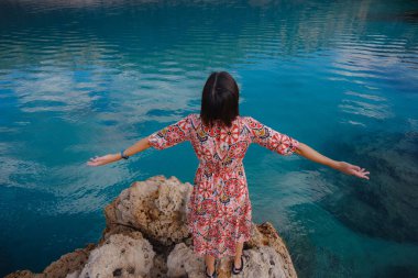 Kadın Akdeniz kıyısında duruyor, soğuk, sezon dışı atmosferi kucaklıyor kıyıya vuran dalgalar ve yukarıdaki bulutlu gökyüzü. Sakin, sakin bir sahilde huzurlu bir an..