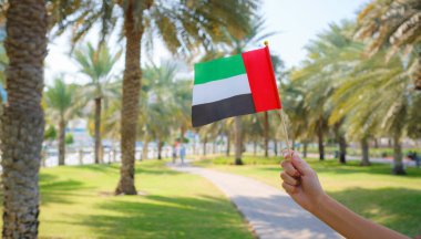 Corniche 'den Abu Dabi Parkı' na karşı küçük bir BAE bayrağı taşıyan kadın eli. Abu Dabi 'de gezinti. Birleşik Arap Emirlikleri, Orta Doğu. BAE ulusal kutlama ruhunun fotoğrafı..
