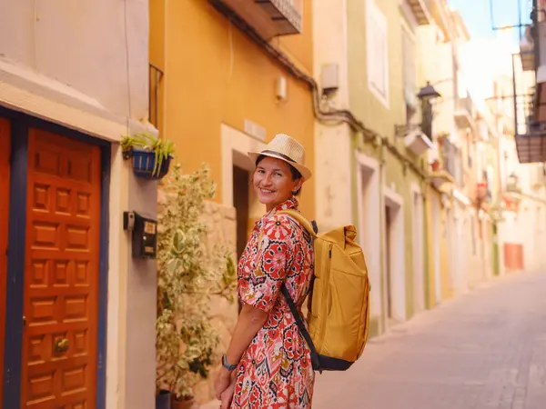 İspanyol kıyı kasabası La Vila Joiosa ya da Villajoyosa 'nın renkli caddelerinde gezen kadın. Güneşli kış atmosferi Akdeniz mimarisinin ve sakin deniz yaşamının cazibesini vurguluyor