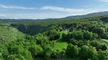 Korana nehri Plitvice yakınlarındaki yeşil tepelerden akar. Korana Nehri 'nin tepeler ve ormanlar boyunca kıvrımlı manzarası. Sıcak güneş ışığı ve Hırvat kırsalının zengin dokularına sahip taze bahar manzarası