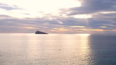 Cala Tio Ximo kıyı şeridi Aralık akşamında ele geçirildi. Sakin kış denizi, yumuşak gün batımı parıltısı, Benidorm yakınlarındaki küçük adanın huzurlu manzarası. Sessiz doğal güzellik, insan yok, sadece deniz ve gökyüzü..