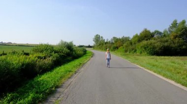 Kırsal alanlarda yürüyüş yapan bir kadın, açık araziler, temiz hava ve huzurlu kırsal manzarayla çevrili. Açık havanın doğal güzelliğini ve sükunetini seviyor..