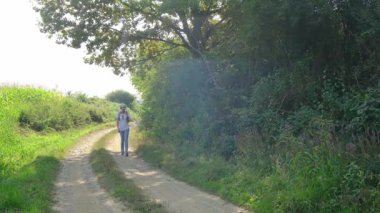 Kırsal alanlarda yürüyüş yapan bir kadın, açık araziler, temiz hava ve huzurlu kırsal manzarayla çevrili. Açık havanın doğal güzelliğini ve sükunetini seviyor..