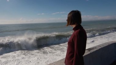 Türkiye 'nin Antalya kentinde fırtınalı Akdeniz kıyıları yakınında duran genç bir kadın. Güneşli kış günü, güçlü dalgalar, rüzgarlı saçlar, derin düşünceler. Doğayla barışçıl ama dramatik bir bağ anı..