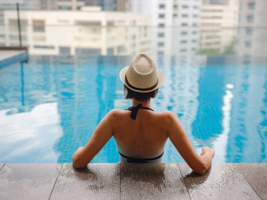 Kuala Lumpur Oteli 'nde havuz başında dinlenen Asyalı genç bir kadın. Etrafı gökdelenlerle çevrili, hareketli şehir ortamında boş vakitlerin tadını çıkarıyor..