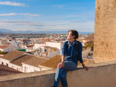 Denia, Alicante, İspanya 'da tarihi şatoyu keşfeden genç bir kadın, aşağıdaki kasabanın manzarası, daha serin mevsim arkaplanlarına karşı. Tarihin ve sükunetin zamansız ortamında harmanlanması.