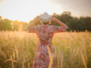Yaz sonlarında Avrupa 'nın pitoresk alanlarında yürüyen genç bir kadın. Altın güneş ışığı, yemyeşil yemyeşil ve sakin kırsal atmosfer huzurlu bir kırsal alan yaratır..