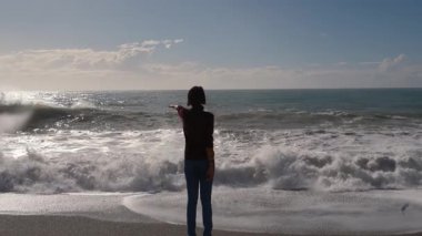 Türkiye 'nin Antalya kentinde fırtınalı Akdeniz kıyıları yakınında duran genç bir kadın. Güneşli kış günü, güçlü dalgalar, rüzgarlı saçlar, derin düşünceler. Doğayla barışçıl ama dramatik bir bağ anı..